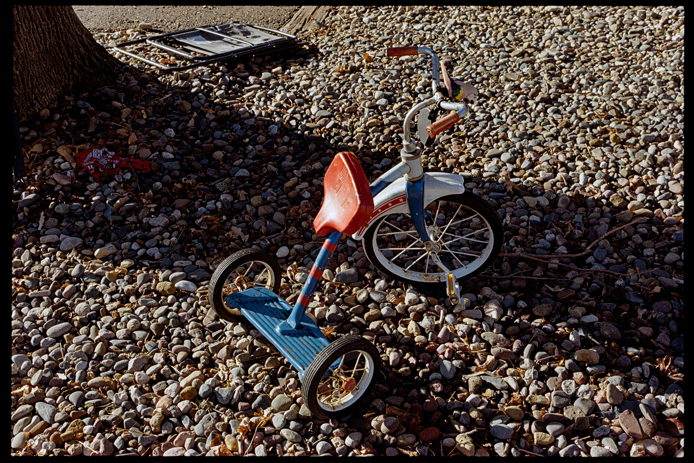 Red, white, and blue tricycle on a gravel driveway