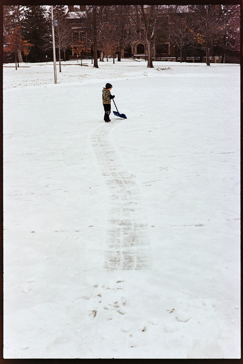 Ethan the young boy shoveling a path through the snow on an outdoor ice rink