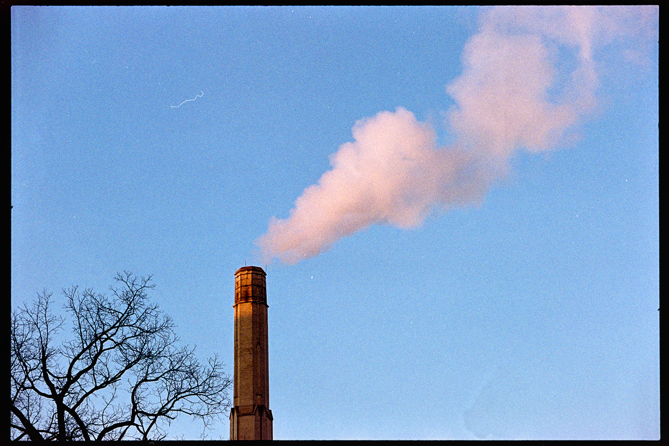 Smokestack billowing white steam in the golden red light of the evening
