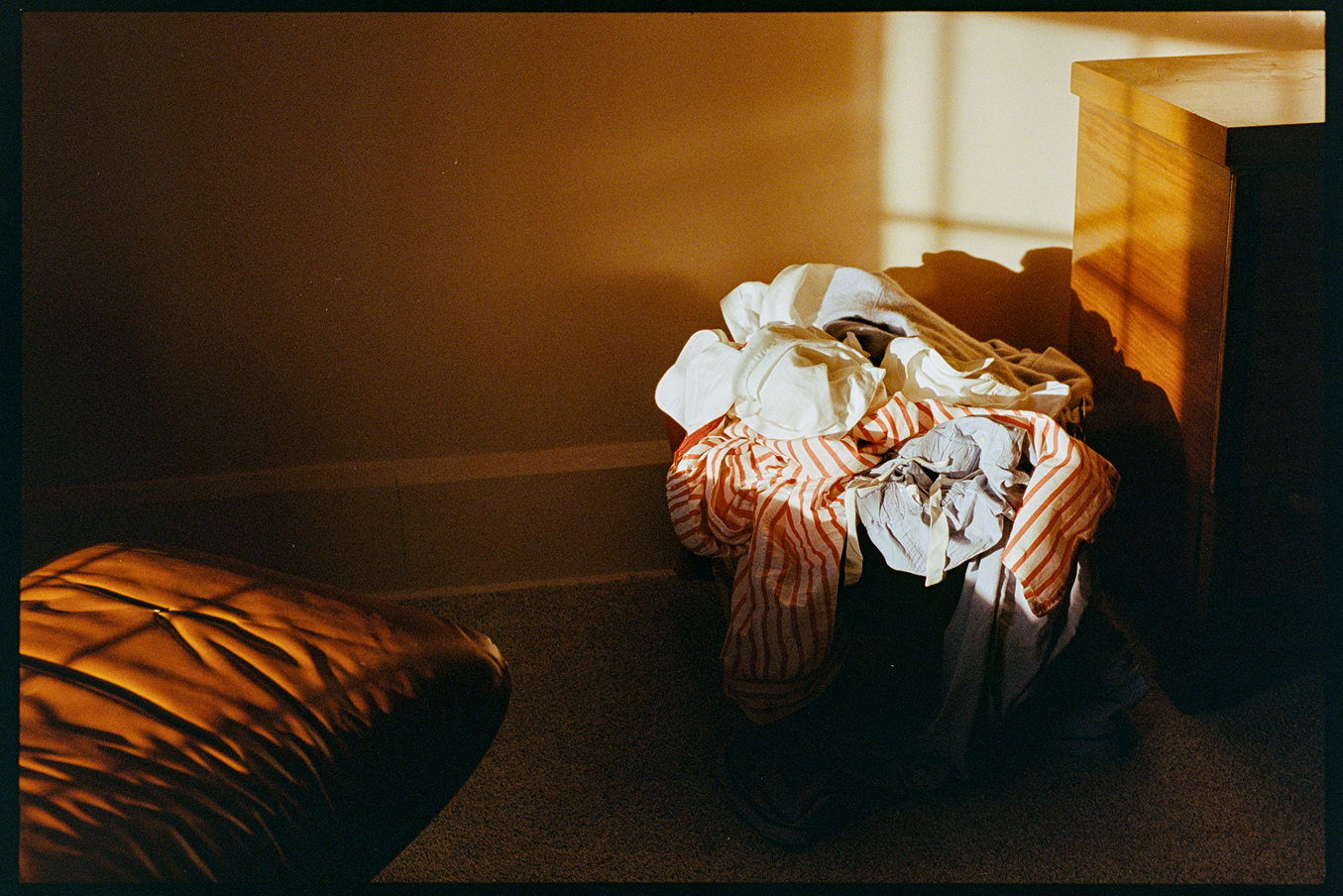 Chair, ottoman, laundry basket in a bedroom with afternoon light coming in through the window