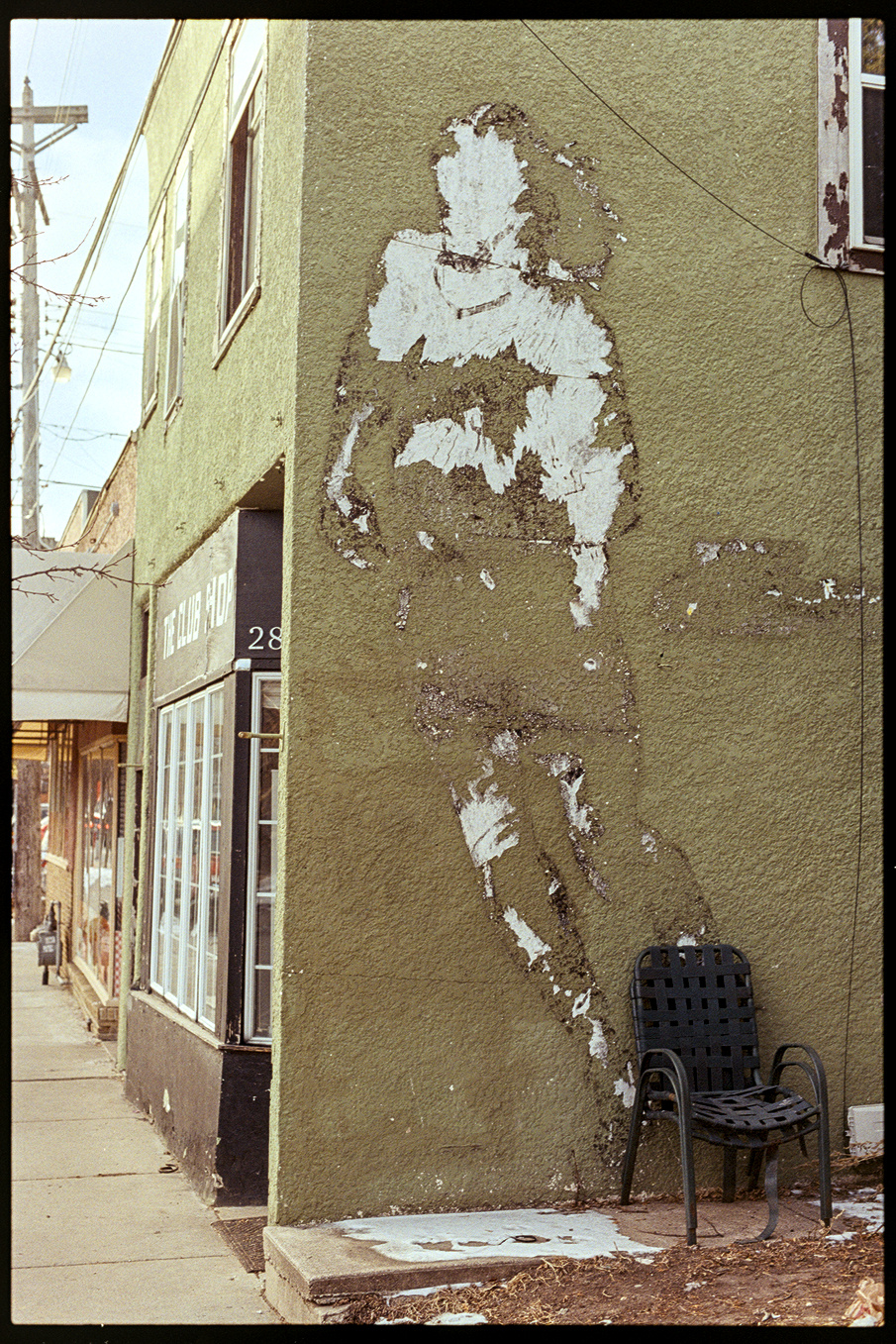 The side of a green building with the two-story silhouette of a soccer player that used to be painted on the wall