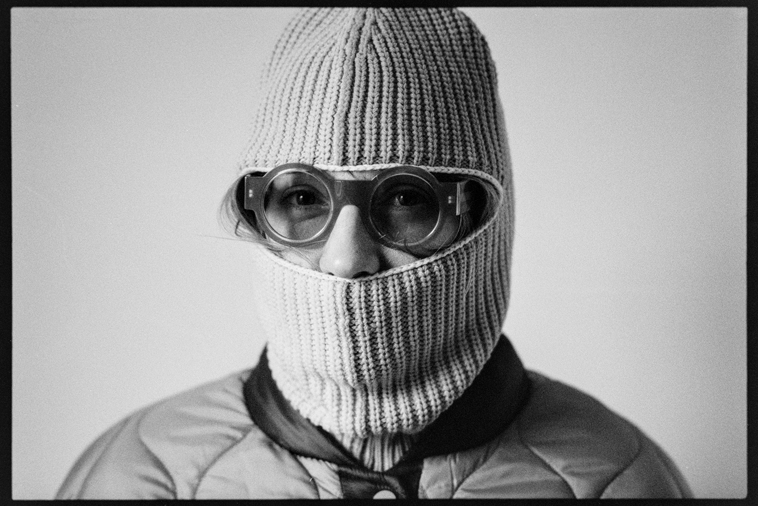 Kallie in a ski mask and round sunglasses looking at the camera