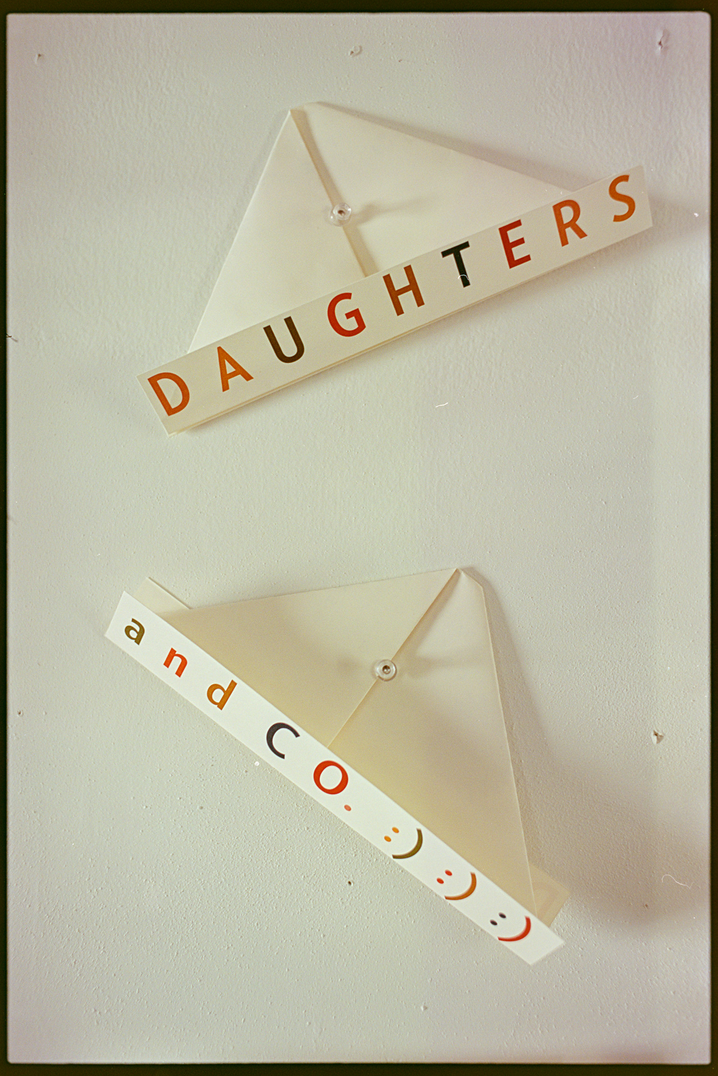 Paper hats pinned to a white wall that say Daughters and Co