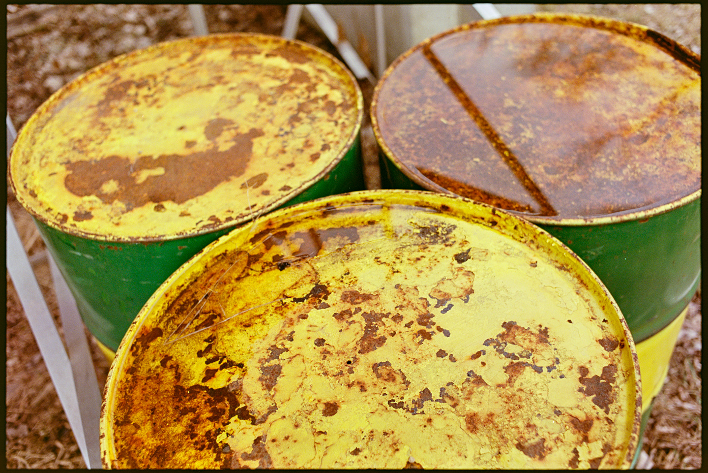 Three large metal barrels under the bleachers, green and yellow with rust and standing water