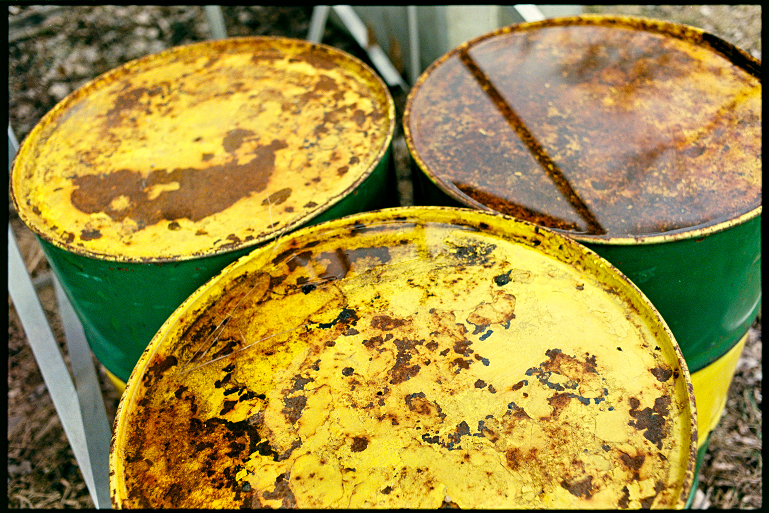 Three large metal barrels under the bleachers, green and yellow with rust and standing water