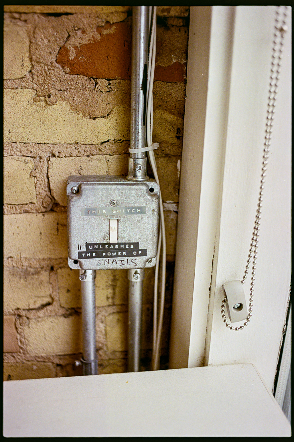 A lightswitch on a brick wall with a label that says 'This switch unleashes the power of snails'
