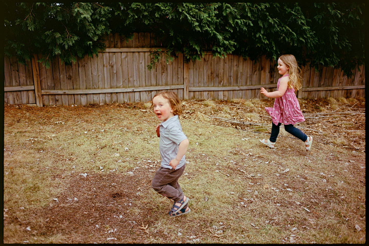 Two children, Ned and Poppy, running in the backyard at a cookout