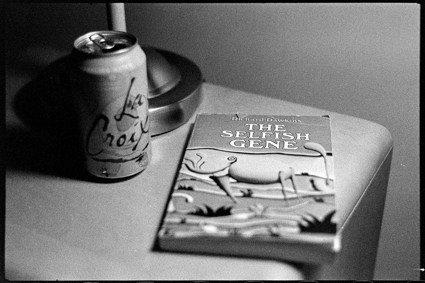 The Selfish Gene book on the night stand with a can of La Croix