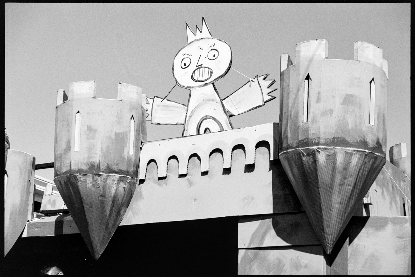 A cardboard king wearing a crown looks down from his cardboard castle at the No Kings Mayday Parade