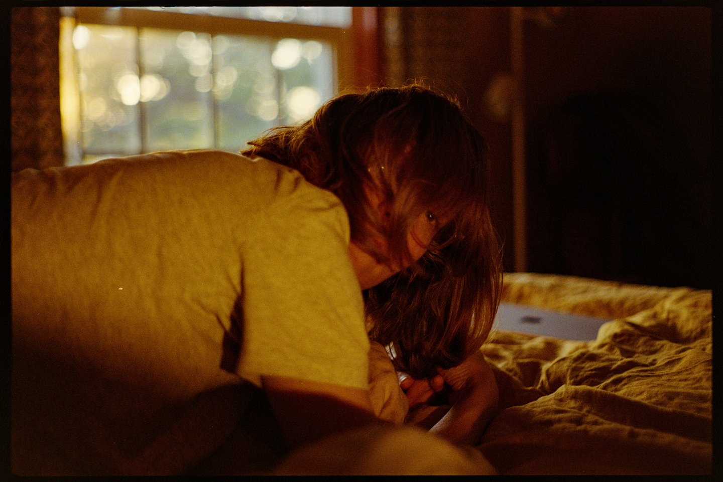 Kallie laying on her stomach in bed with golden evening light coming in from the window behind her