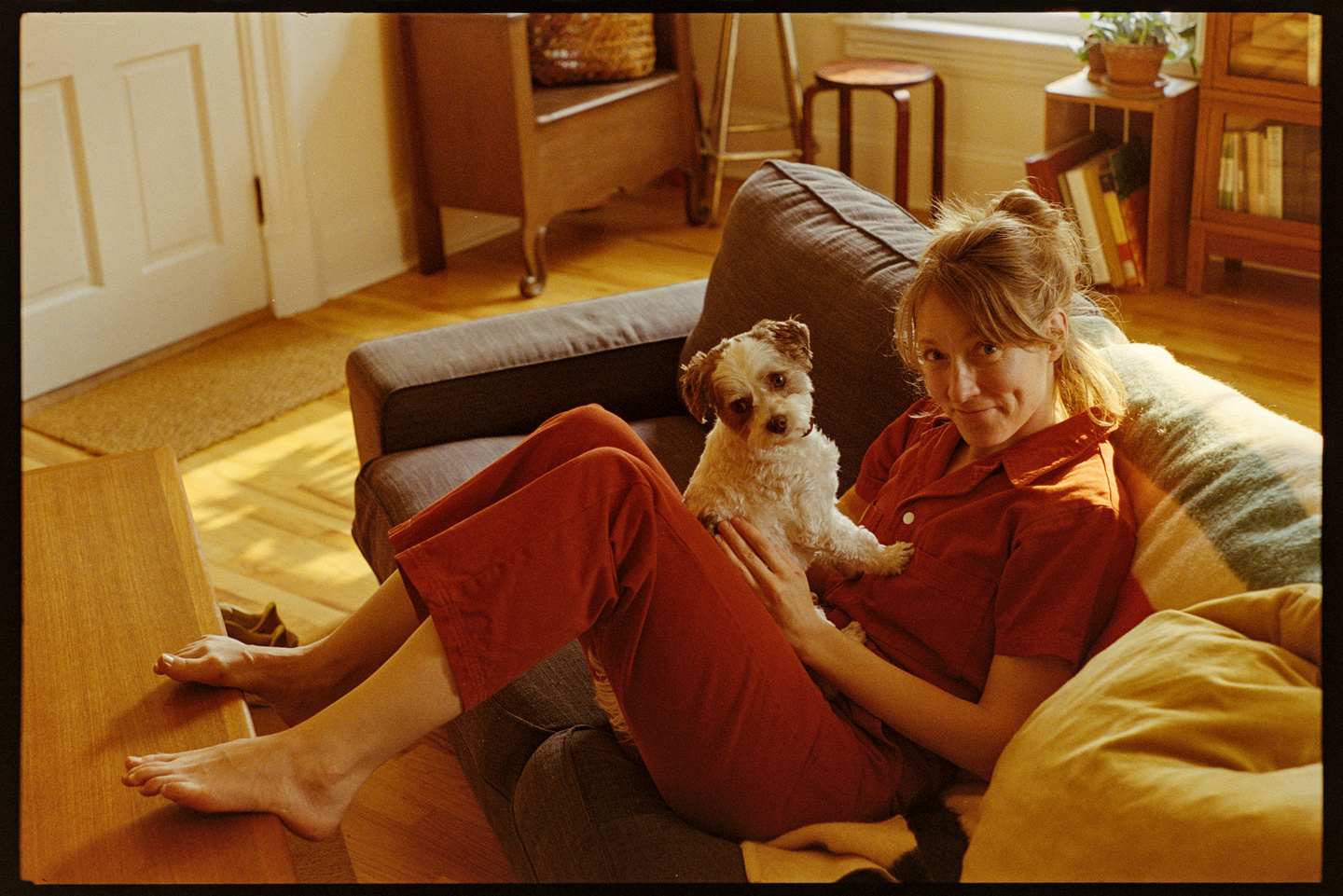 Kallie in a red jumpsuit sitting on the couch with her dog Annie on her lap