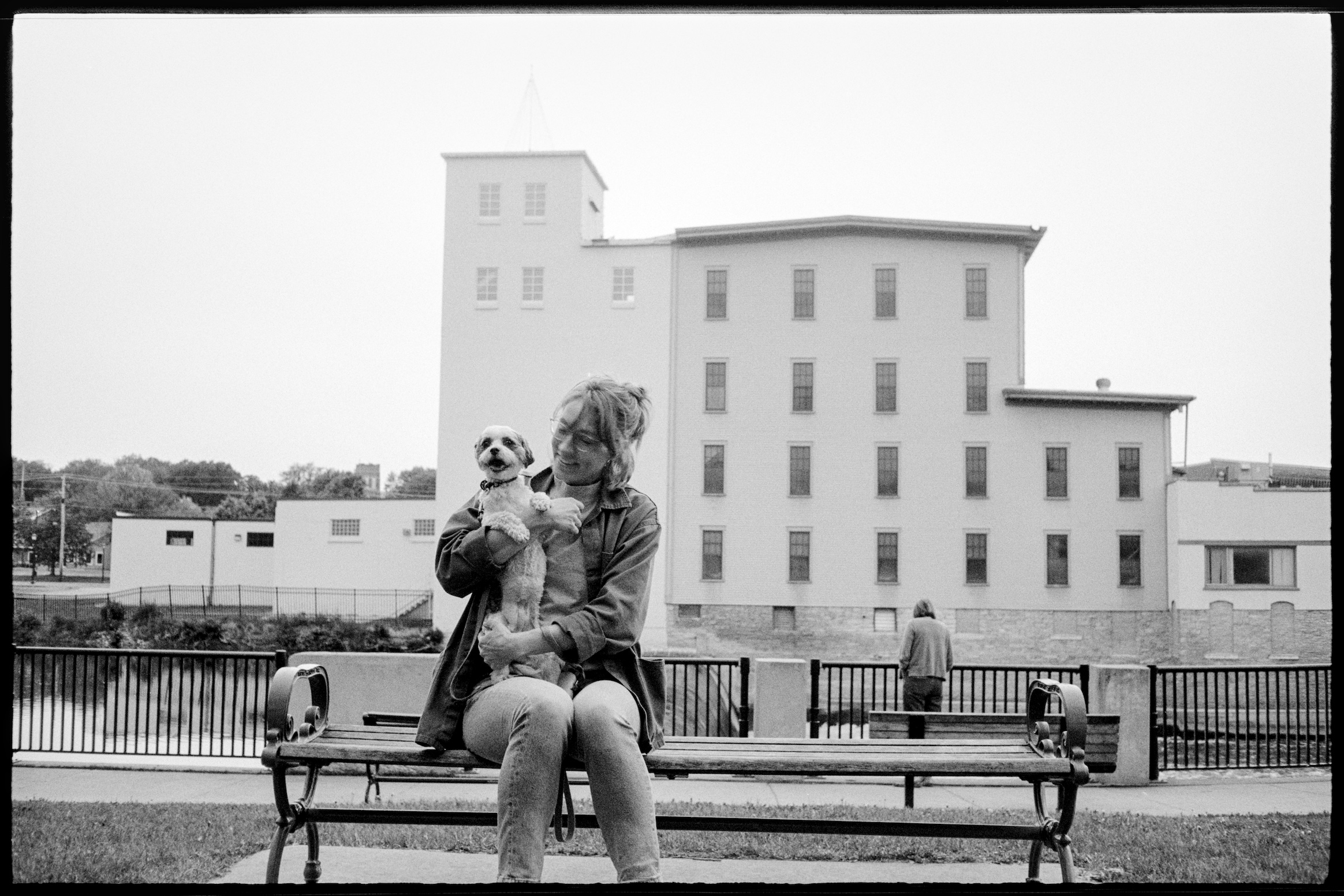 Kallie holding Annie, sitting on a bench in front of the Cannon River and Ames Mill