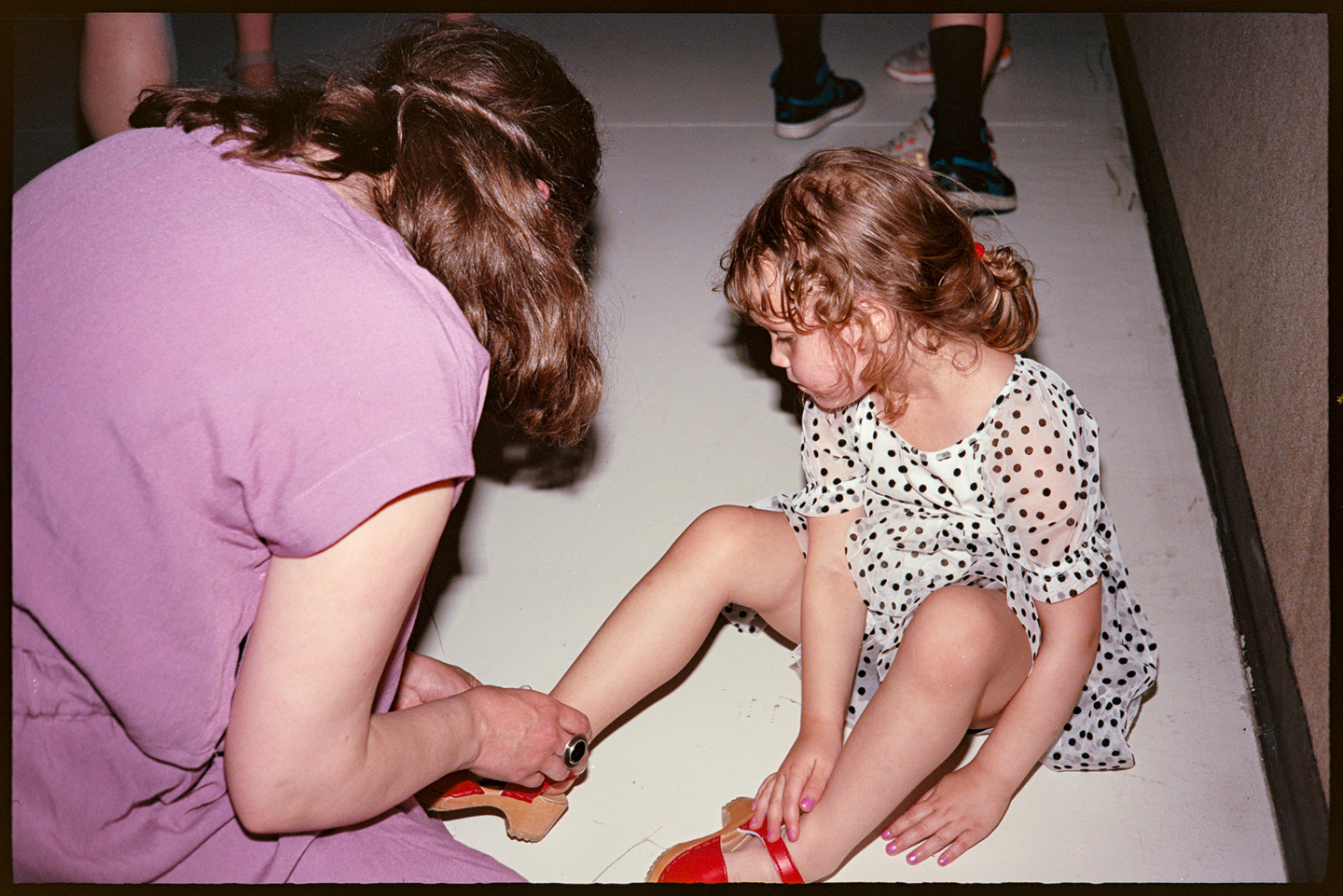 Courtney bent over fixing her daughter Suvi's red shoes at a wedding reception