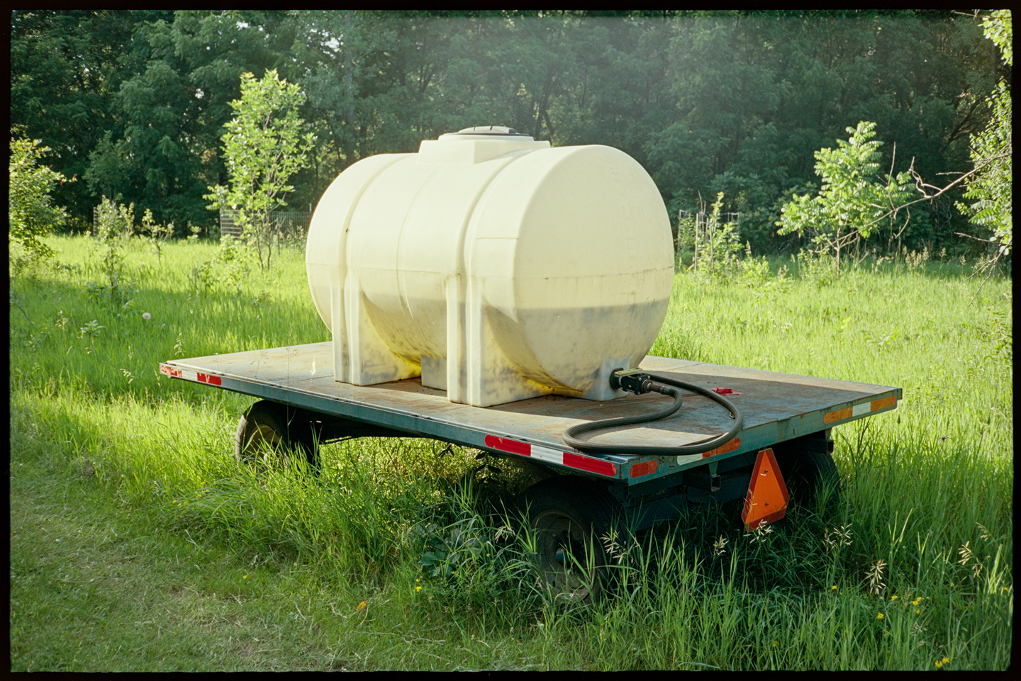 A large tank of water on a trailer bed along a path in an arboretum