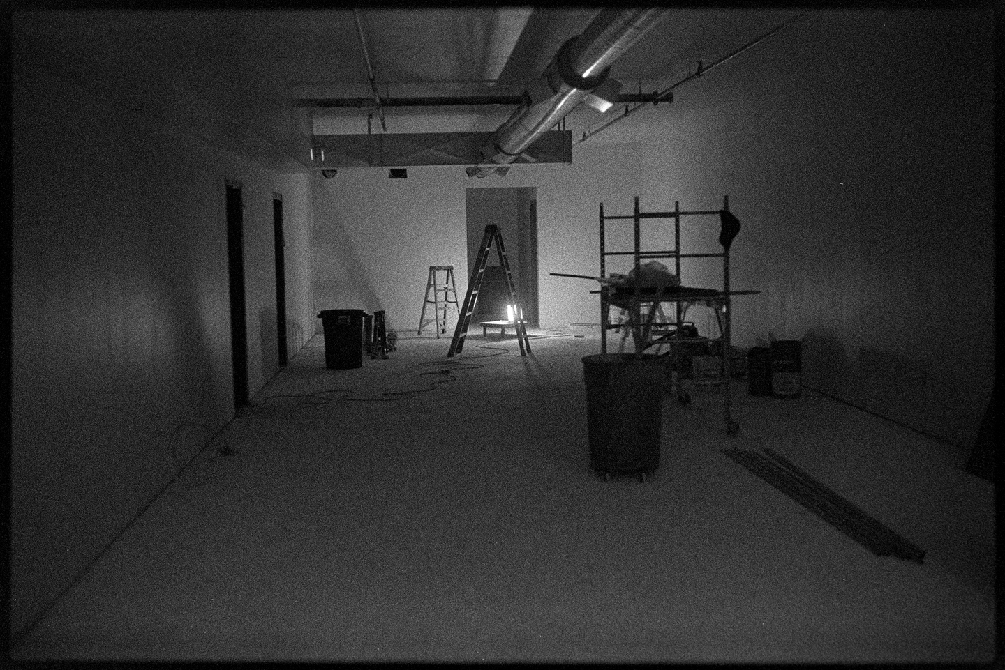 An empty retail space in darkness except for a lamp on the floor and a ladder