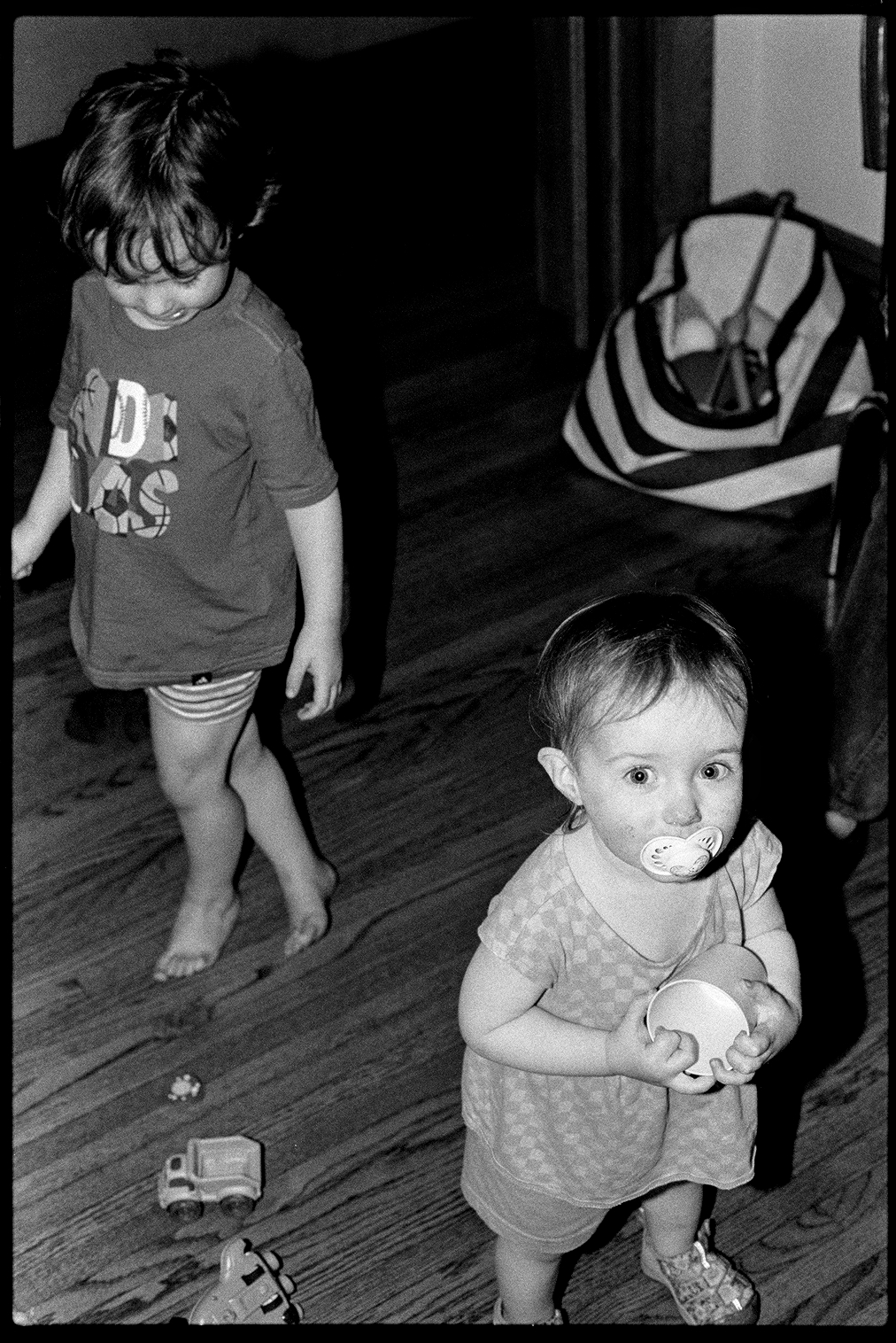 Two toddlers, a boy and a girl, walking around their family room