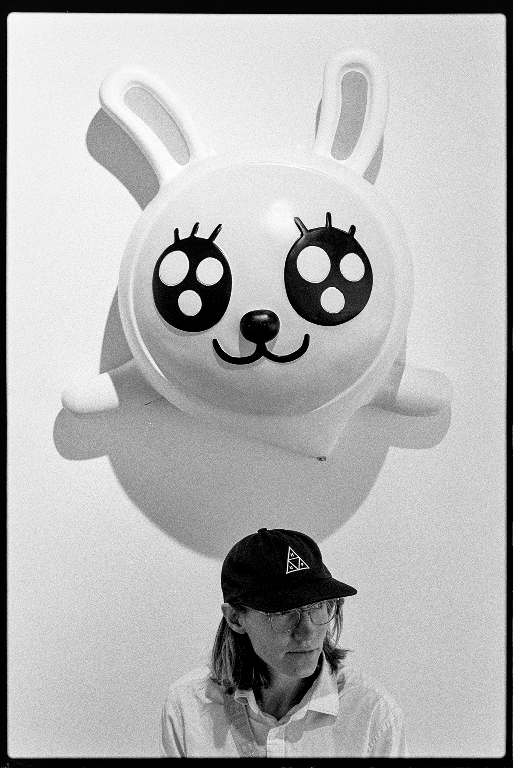Kallie sitting under a sculpture of a cartoonish white rabbit mounted on the wall at a claw machine parlor