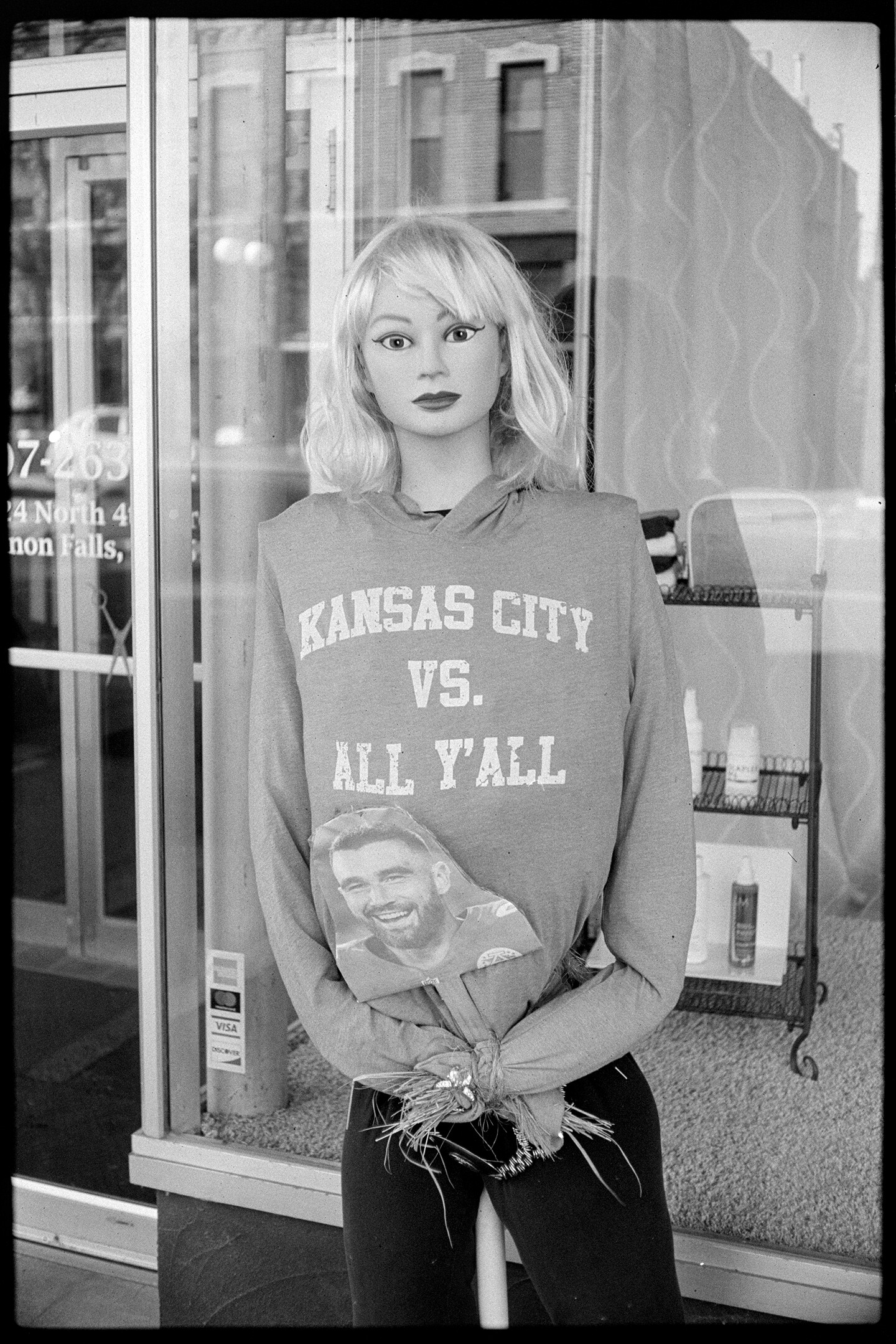 Mannequin dressed as Taylor Swift wearing a sweater that says 'Kansas City vs All Y'All' and holding a photo of Travis Kelce