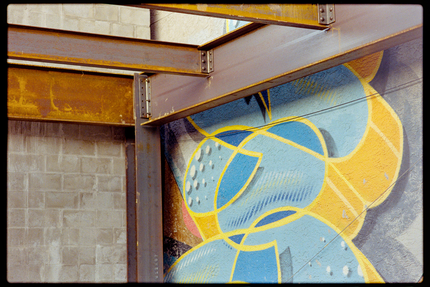 Steel beams of a building being constructed in front of a wall of bright blue and orange graffiti