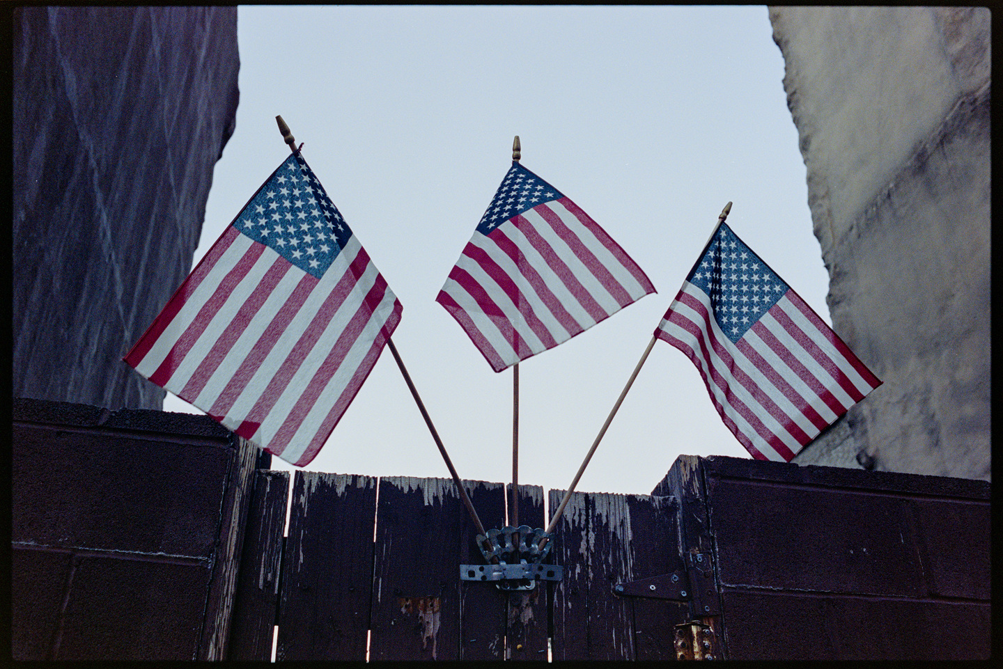 Three small American flags mounted on a wooden fence between two buildings