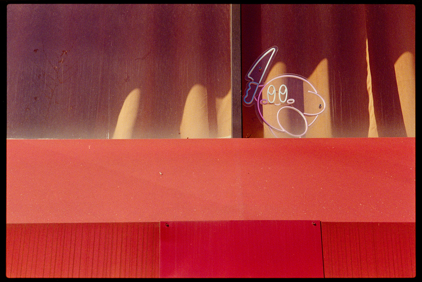 A small neon sign of Kirby running with a knife, mounted in someone's apartment window