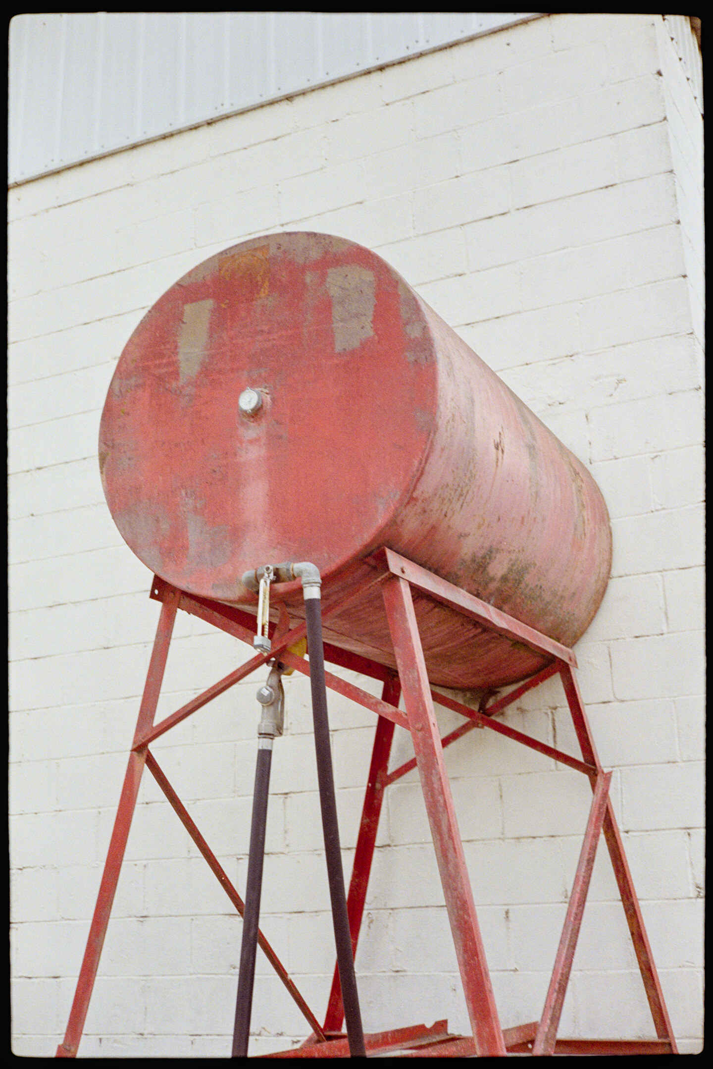 A red gas tank in front of a white building
