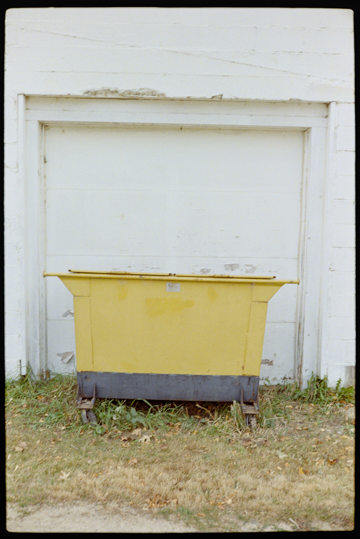 A yellow dumpster in front of a white building across from the Oak Center