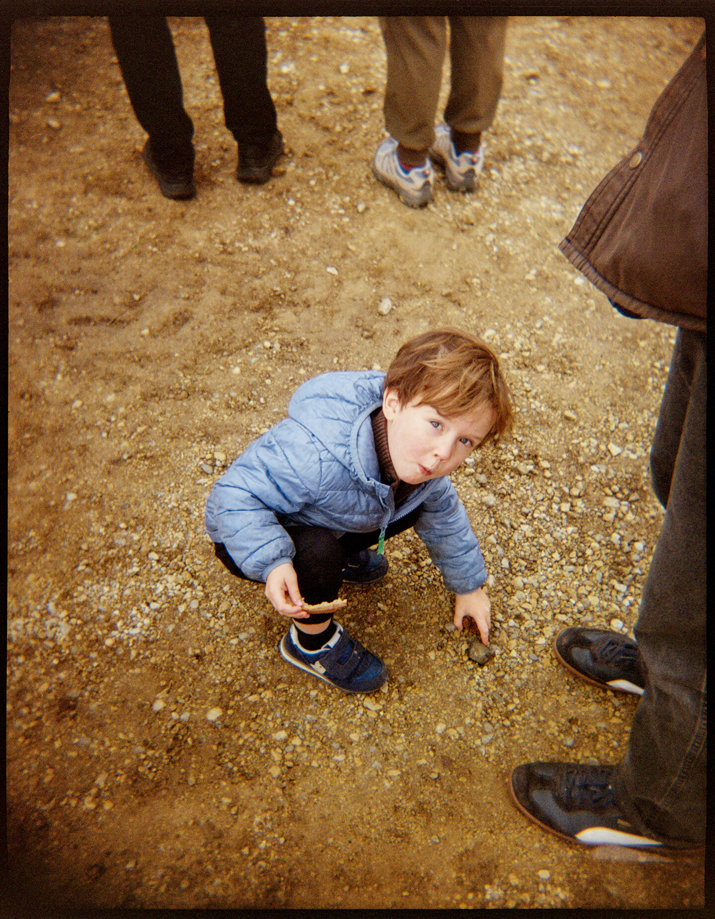 A young boy eating bread and crouching on the ground next to an adult