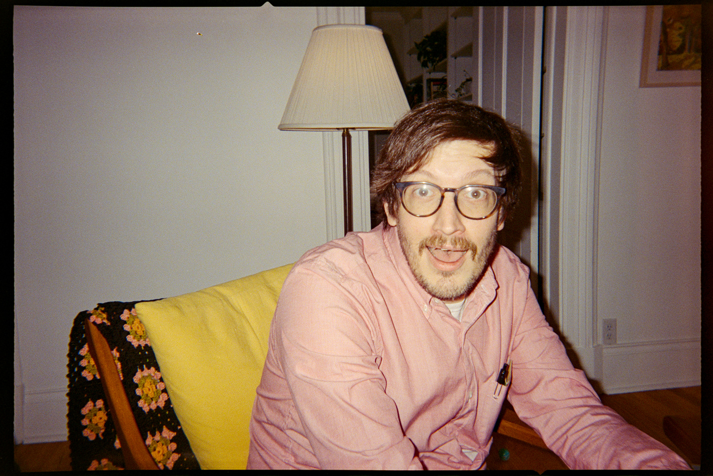 A man sitting in an armchair looking at the camera with a goofy face.