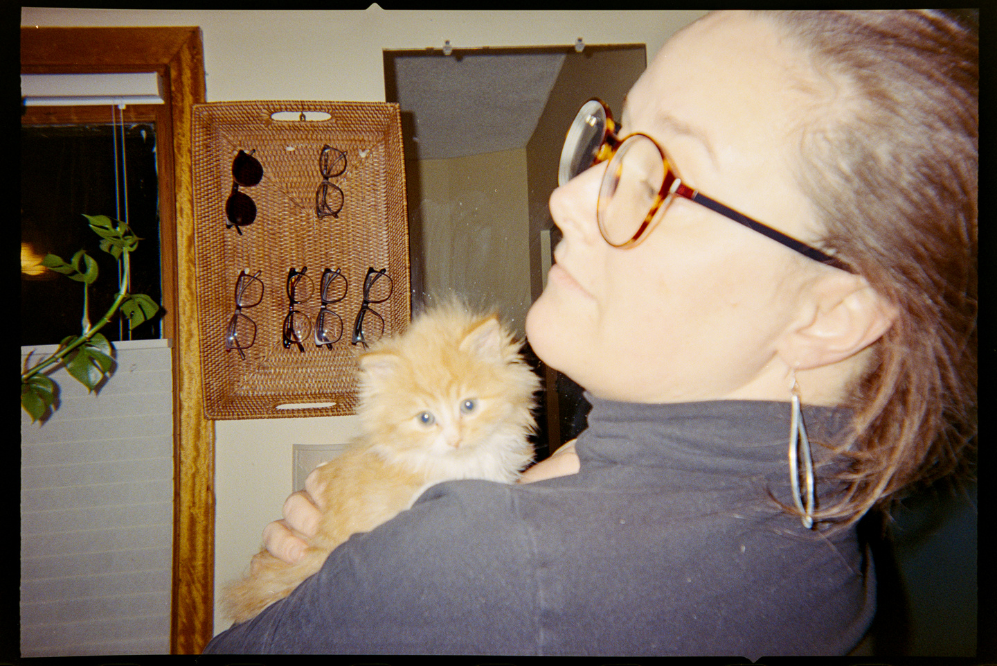 A woman in a black turtleneck shirt with a tiny orange kitten on her shoulder.