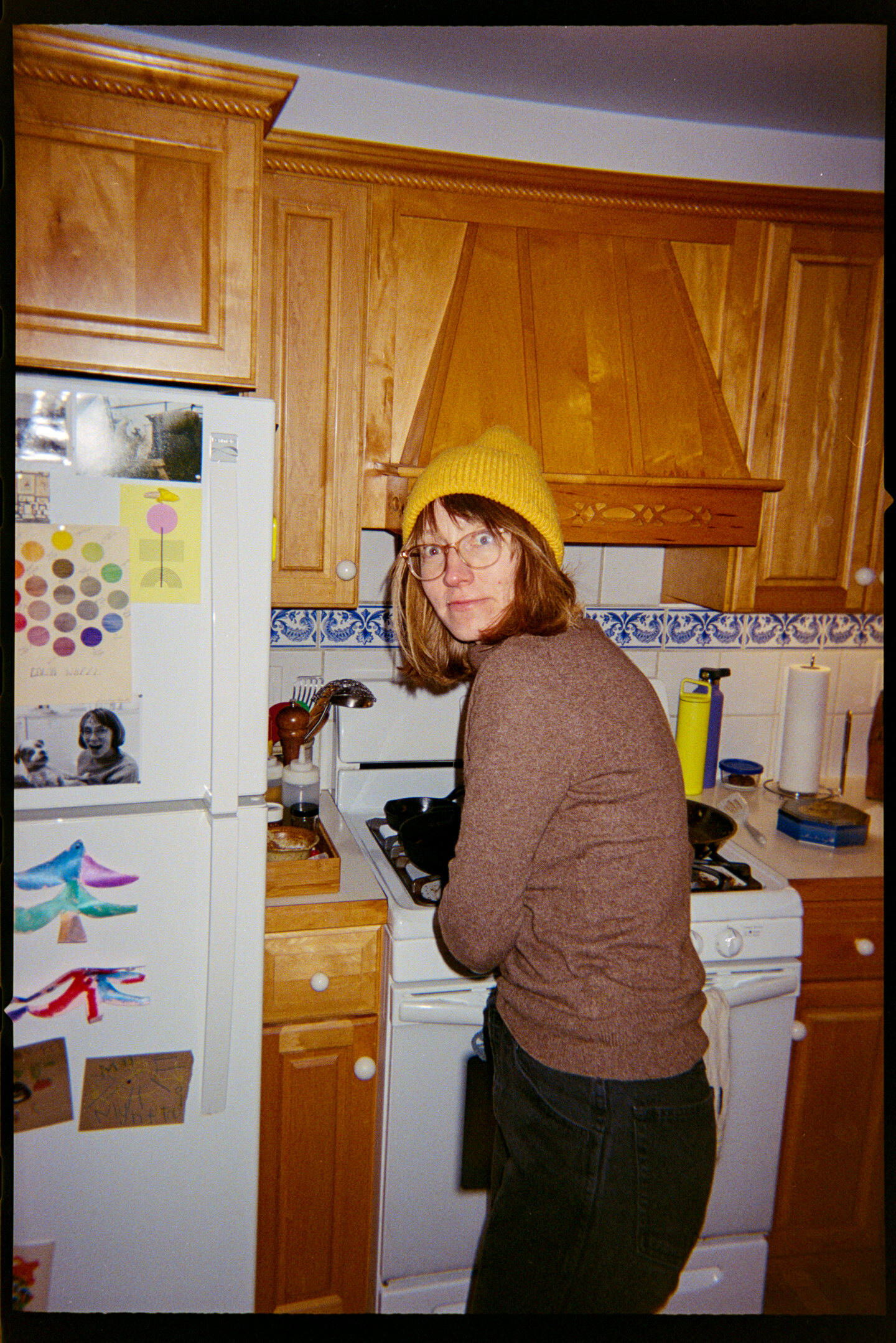 A woman in a yellow snow cap standing in front of an oven looking back over her shoulder at the camera.