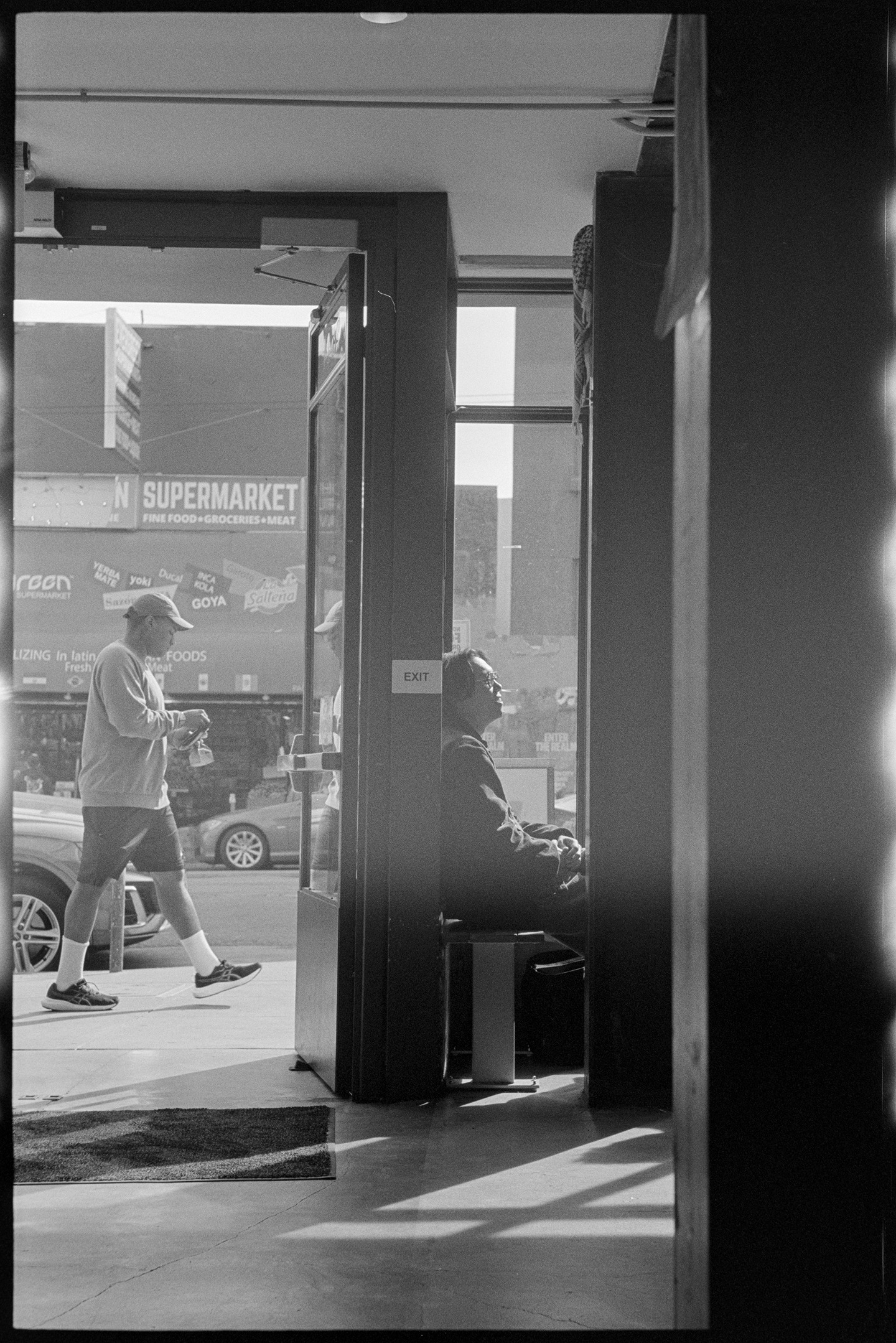 A man sitting in the front window of a coffee shop while another man walking on the sidewalk in the background