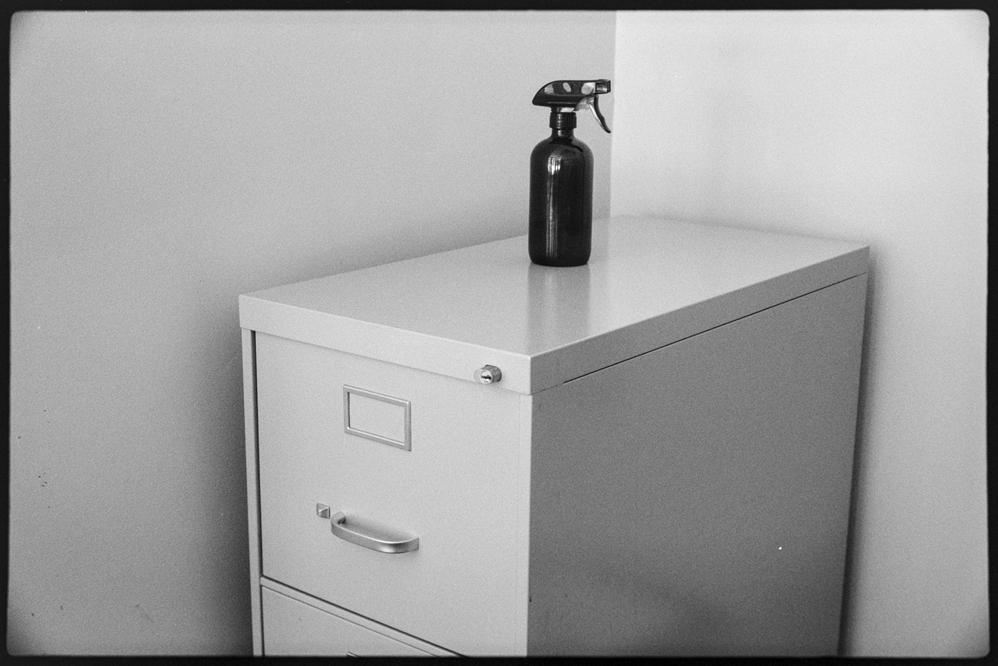 Dark spray bottle on top of filing cabinet in a corner