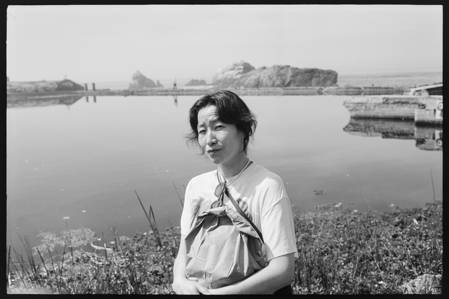 A woman holding a bag of bagels and looking at the camera in front of a pool of water at Sutro Baths