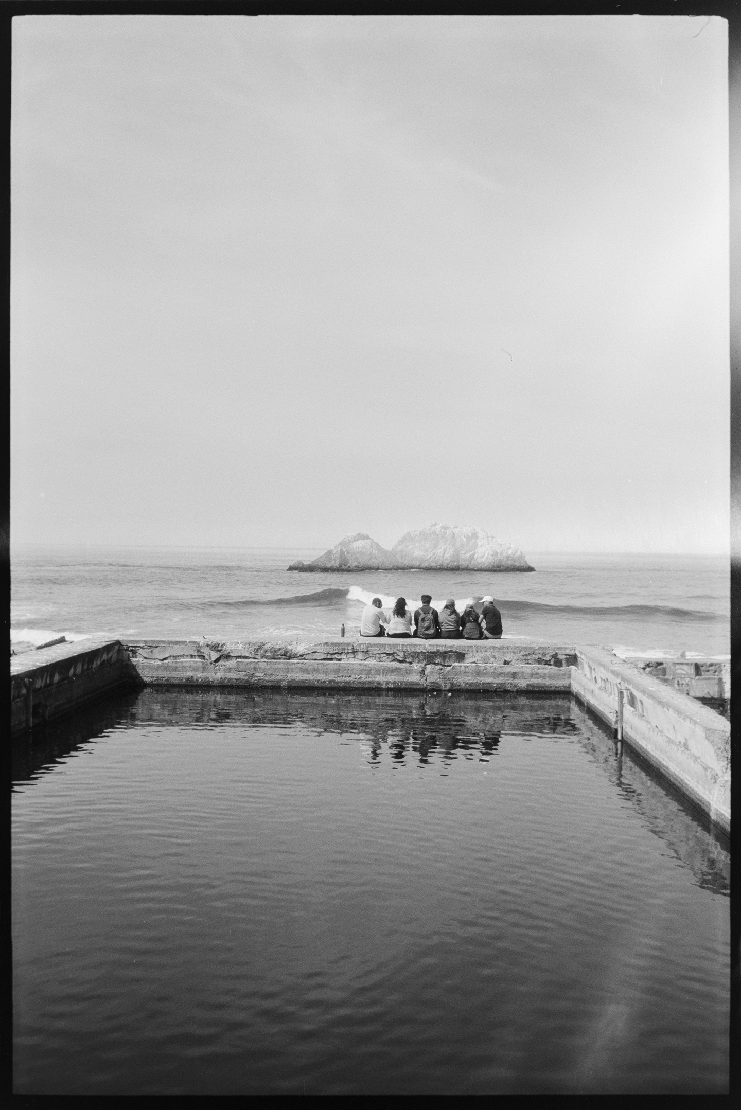 A family sitting on the edge of a pool looking out at the Pacific coast at the Sutro Baths