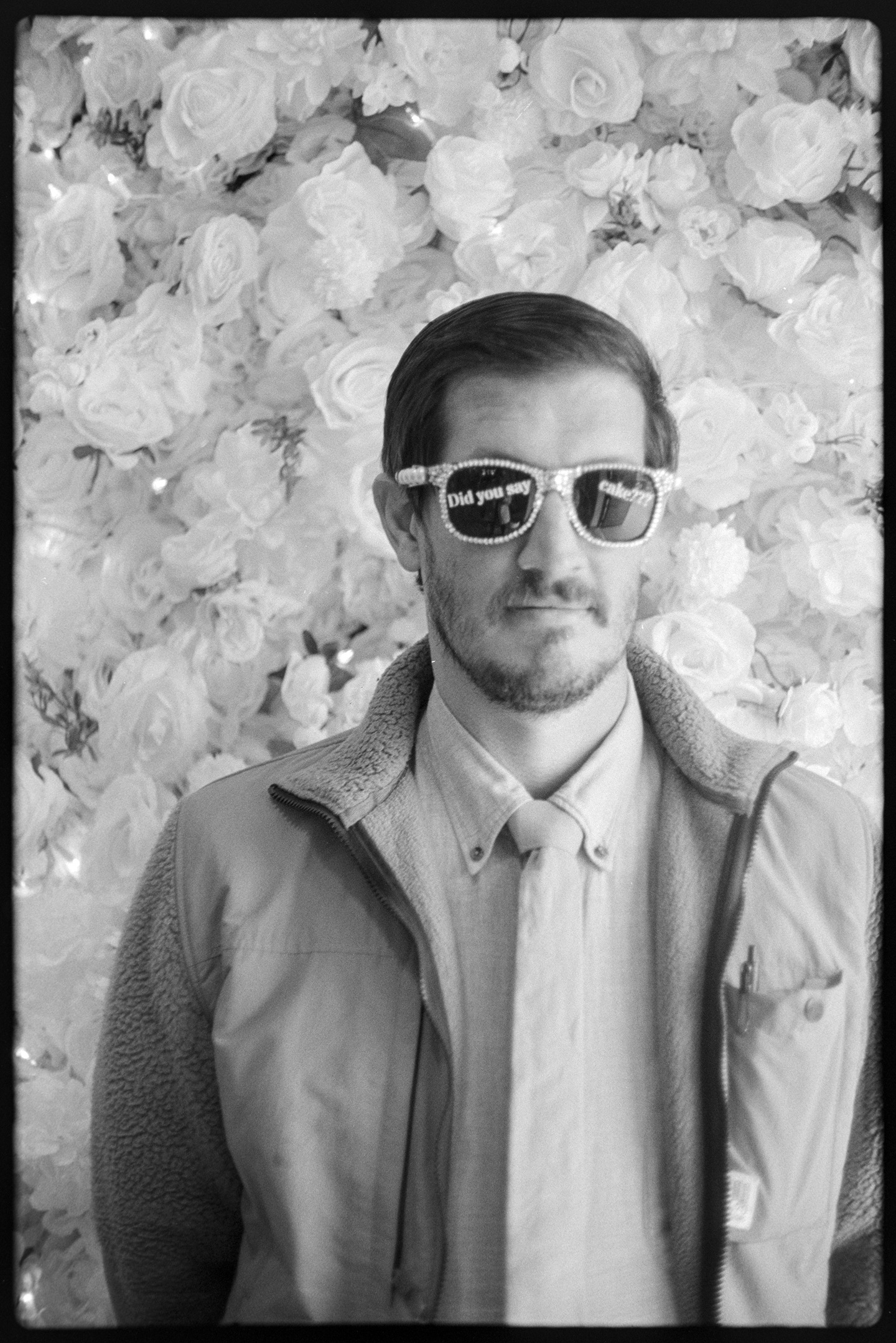 Jason in front of a wall of flowers and wearing sunglasses that say 'Did you say cake?'