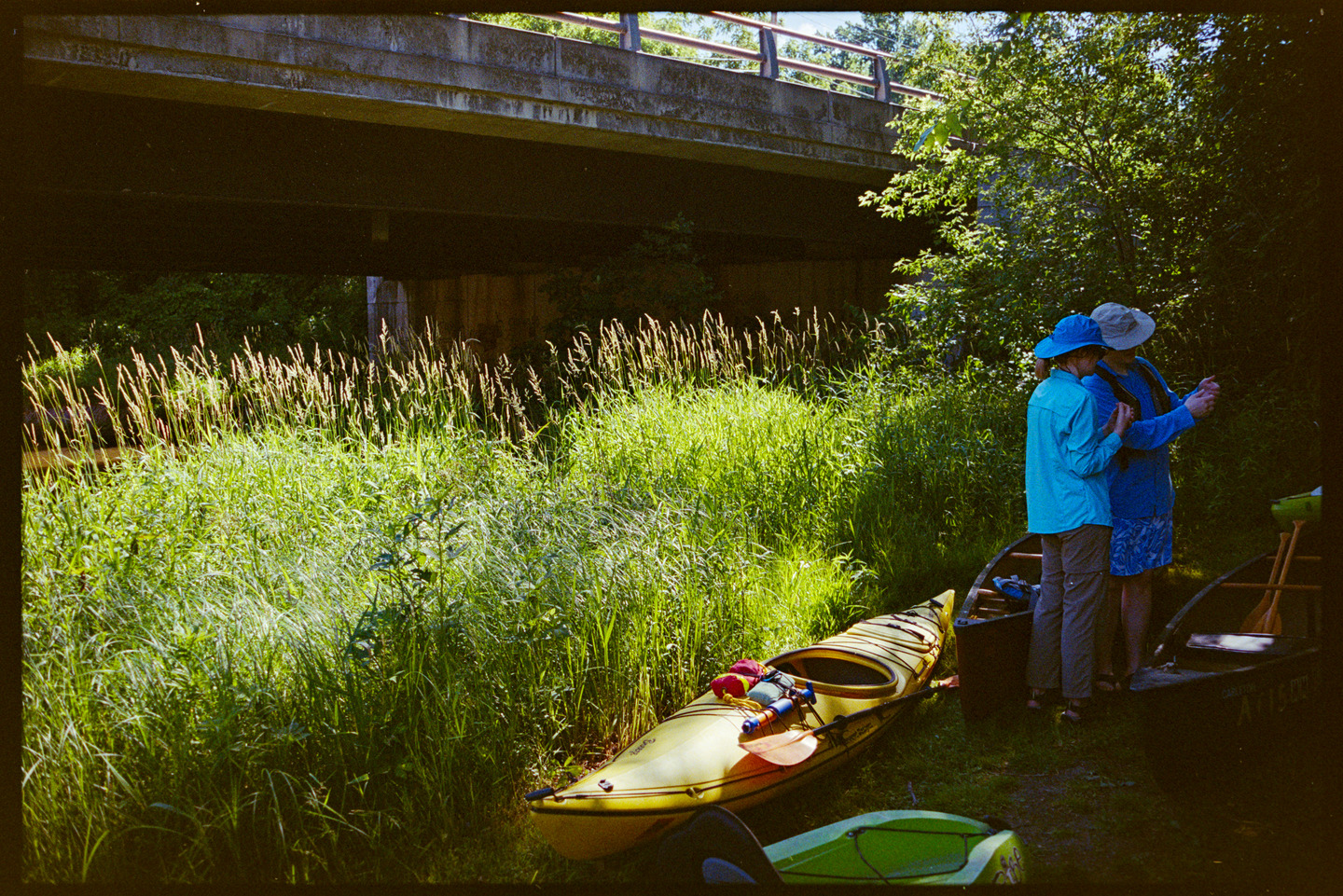 Two women preparing for a kayak trip on the Cannon River next to a concrete bridge