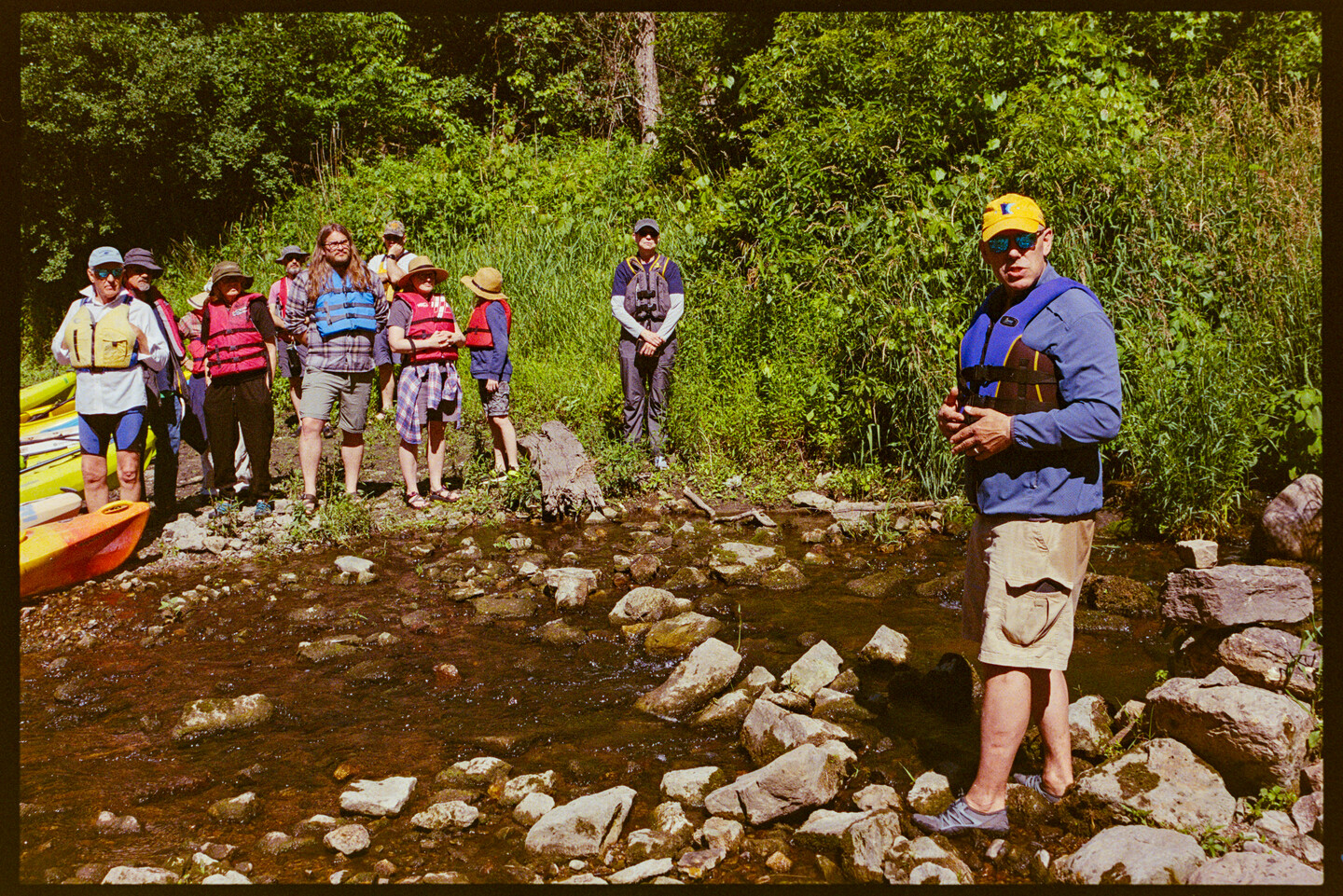 A group of people have stopped on a creek that leads into the Cannon River. A man explains to the group the importance of water quality in rural Minnesota and the water habitats that are impacted