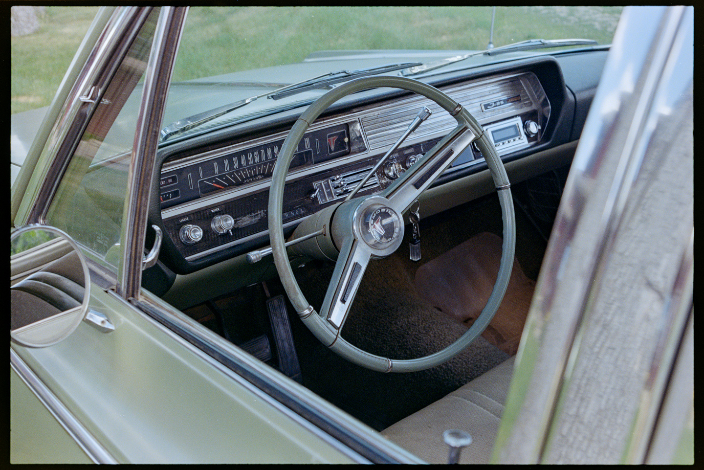 Looking through the driver side window into a 1960s Oldsmobile, seeing the steering wheel and dashboard